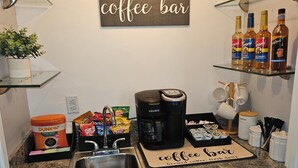 A kitchen with a coffee bar sign, a Keurig coffee maker, snacks, and a shelf with bottles.