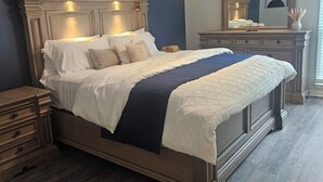 A bedroom with a large bed, a nightstand, a dresser, a ceiling fan, and a mirror.
