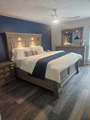 Ein Schlafzimmer mit einem großen Bett, einem Nachttisch, einer Kommode, einem Deckenventilator und einem Spiegel.