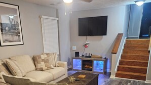 A living room with a sofa, coffee table, fireplace, TV, and a staircase.