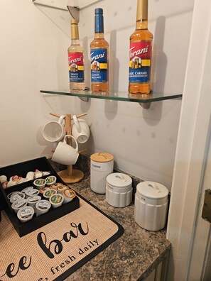 Eine Küchenarbeitsplatte mit Flaschen Torani Sirup, einem Kaffeekrug, Zucker- und Teebehältern, einer Kaffeemaschine und einer Donut-Platte.