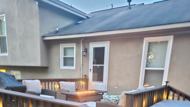 A deck with outdoor furniture, a fire pit, and a house with a beige exterior.