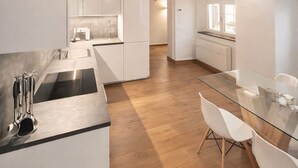 Een moderne keuken met witte kasten, een glazen eettafel en houten balken in het plafond.