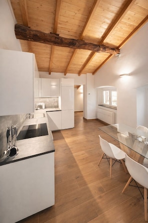 Une cuisine moderne avec des meubles blancs, une table à manger en verre et des poutres en bois au plafond.