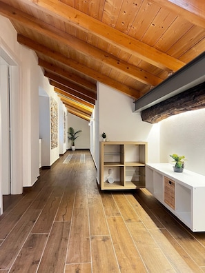 Un couloir doté d’un plancher en bois, d’un plafond en pente et d’une étagère intégrée où est posée une plante.