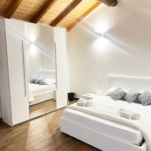 A modern bedroom with a large bed, a wardrobe with a mirror, and a wooden ceiling.