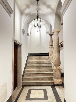Un magnifique escalier en marbre, orné d’un lustre, mène à un plafond en arc de cercle.