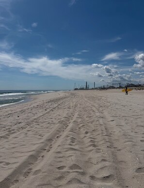 Ein sandiger Strand mit Fußabdrücken, ein klarer Himmel und weit entfernte Vergnügungsparkgebäude.