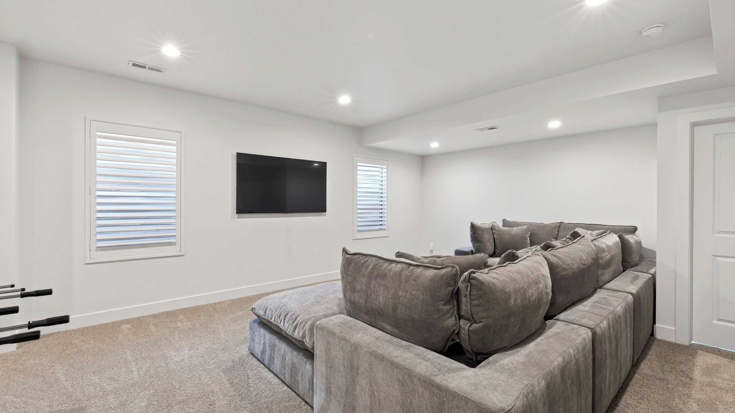 A room with a grey sectional sofa, white walls, a flat-screen TV mounted on the wall, and a door on the right.