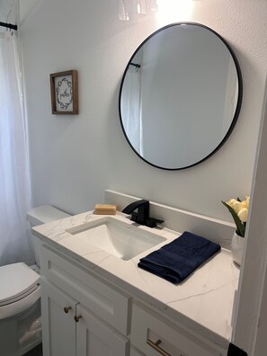Une salle de bain avec un meuble-lavabo blanc, un miroir rond, des toilettes et un petit tableau encadré accroché au mur.