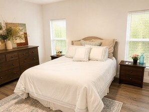 Une chambre à coucher avec un grand lit, une commode, une table de chevet et une fenêtre avec des stores.