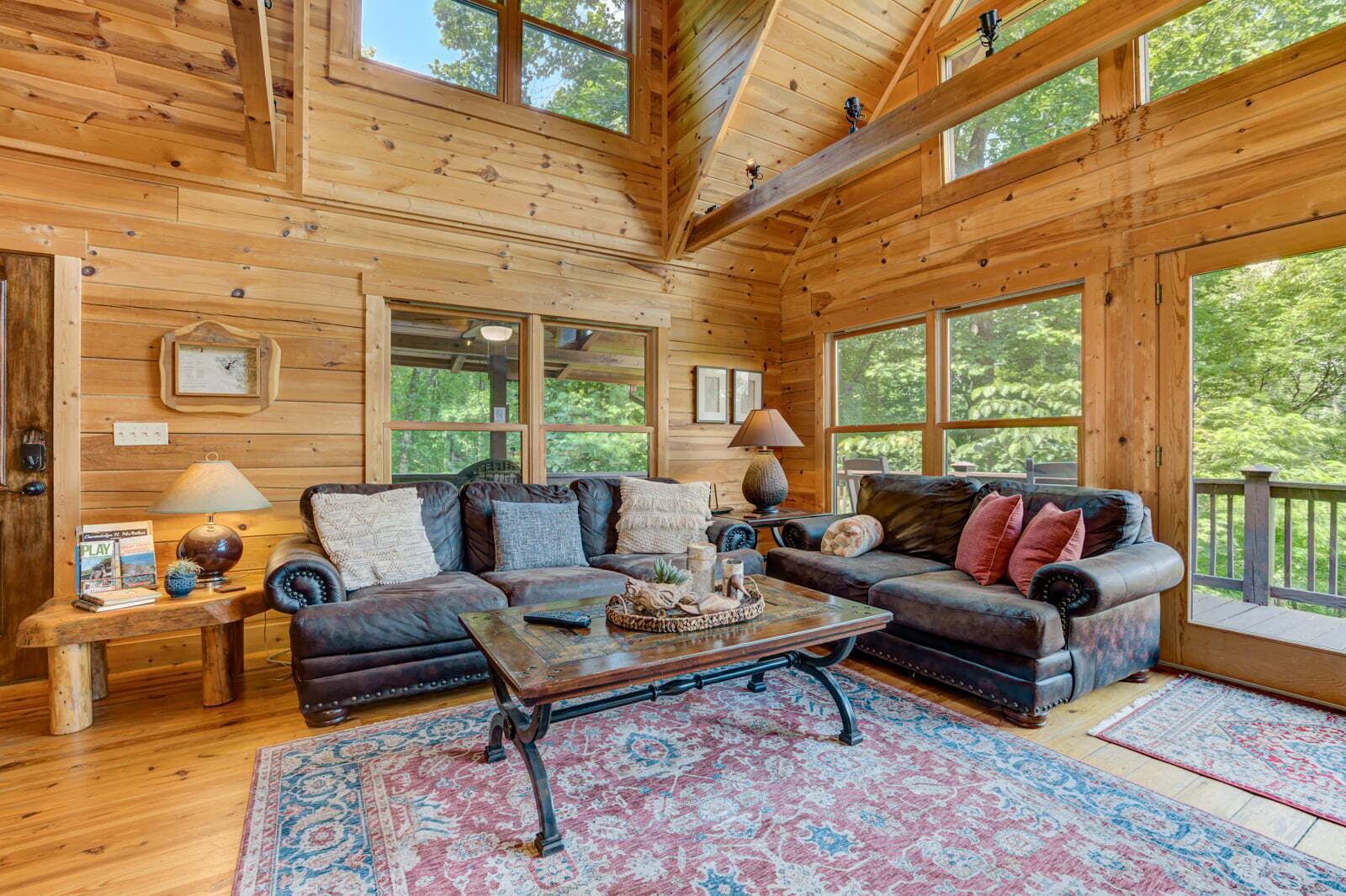 A wooden cabin interior with a large sofa, a coffee table, and a rug.