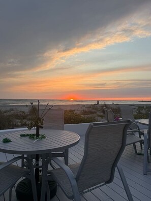 Eine Terrasse mit rundem Tisch und Stühlen mit Blick auf einen Strand bei Sonnenuntergang.