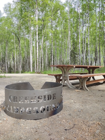 A campsite with a metal fire pit labeled 'CREEP SIDE CAMPING' and a wooden picnic table.. RV Site #1 at Creekside Campground