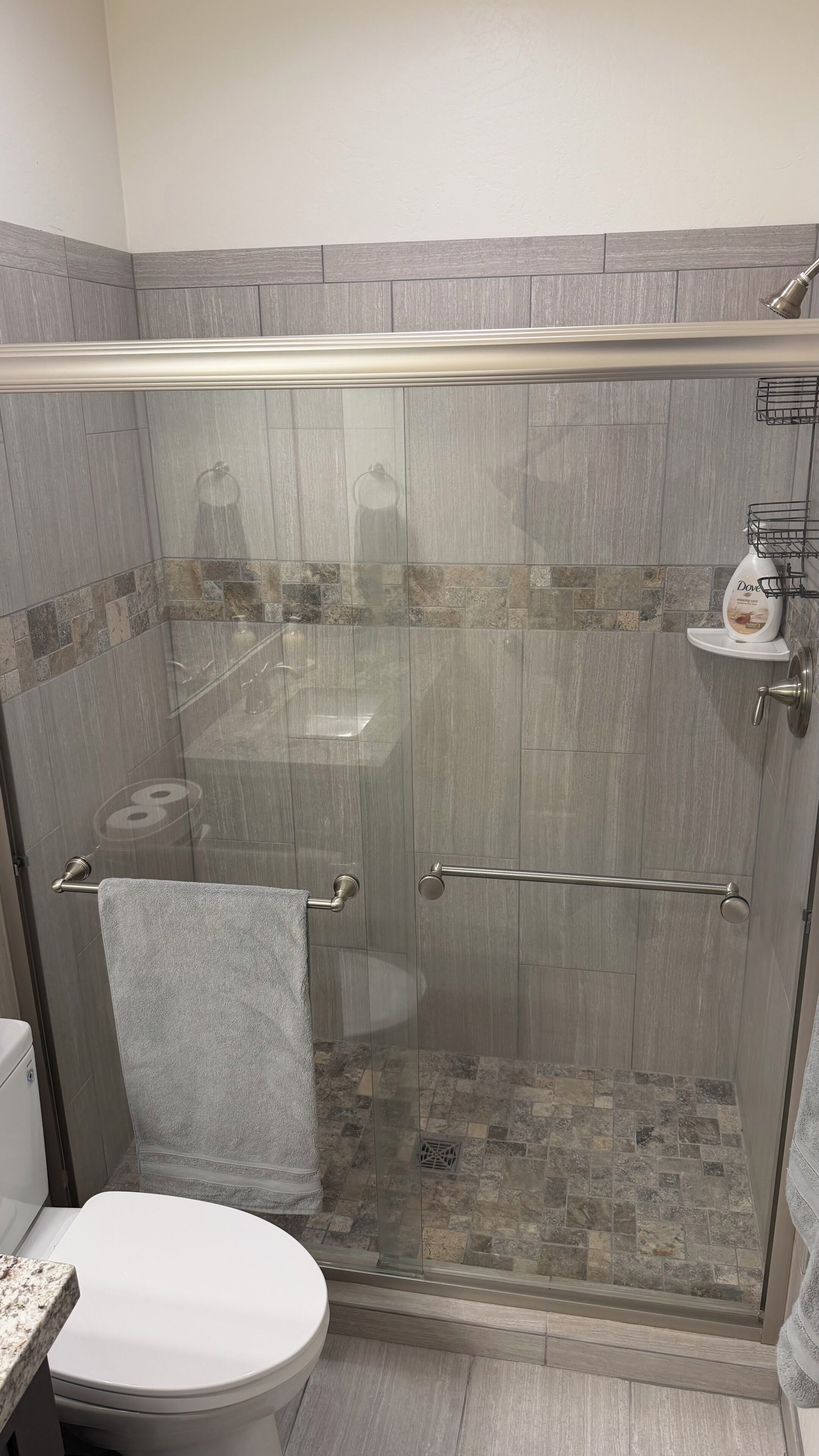 Un espace douche doté d’une porte en verre, d’un porte-serviettes et d’un savonnière.