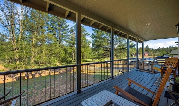 A covered outdoor deck with a view of a wooded area, a fire pit, and seating.