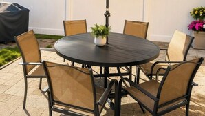A round outdoor table with chairs, an umbrella, and a potted plant. - Spacious 10BD Home - 12 min NYC & MetLife (Bayonne)