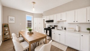 A modern kitchen with white cabinets, a wooden dining table, and a black stove. - Spacious 10BD Home - 12 min NYC & MetLife (Bayonne)