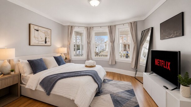 A modern bedroom with a bed, bedside lamps, a TV, and a view of the outside. - Spacious 10BD Home - 12 min NYC & MetLife (Bayonne)