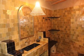 A bathroom with a tiled wall, a sink, a mirror, and a hanging light fixture. - Vrbo Property (Taroudant)