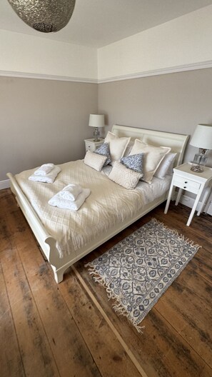 A bed with white bedding and pillows, a bedside table with a lamp, and a patterned rug on a wooden floor. - Minster Panorama is a beautifully restored three story Georgian Town House located on the famous "Th (St Ives)