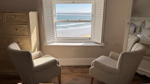 A room with a window overlooking a beach, two armchairs, a wooden dresser, and a bed with patterned pillows. - Minster Panorama is a beautifully restored three story Georgian Town House located on the famous "Th (St Ives)