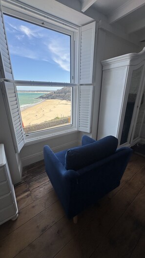 A room with a large window overlooking a beach, a blue chair, and a white cabinet. - Minster Panorama is a beautifully restored three story Georgian Town House located on the famous "Th (St Ives)