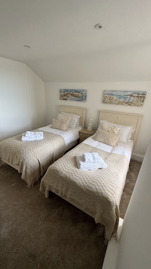 Une chambre d’hôtel avec deux lits, une literie de couleur beige, une table de chevet avec une lampe et deux tableaux accrochés au mur.