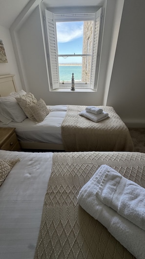 Ein Schlafzimmer mit zwei Betten, einem Fenster mit Meerblick und einem kleinen dekorativen Gegenstand an der Fensterbank.