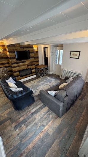 Un salon avec une cheminée, un canapé, une causeuse et un téléviseur fixé au mur.