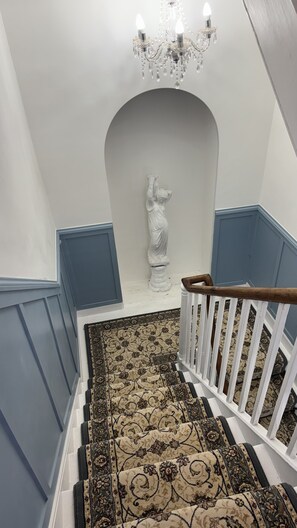 Eine Treppe mit einem gemusterten Teppich, einer weißen Geländer und einer Chandelier.