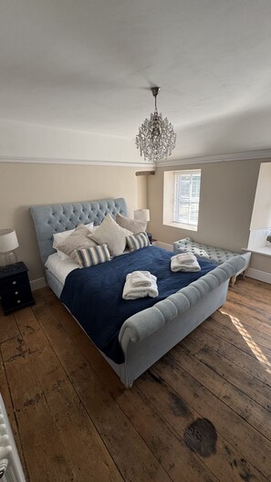 Ein Schlafzimmer mit einem großen Bett, einer Chandelüster, einem Fenster mit Jalousien und einem Holzboden.