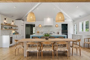 A spacious kitchen with a wooden dining table, white cabinetry, and pendant lights. - 711 Palm - DOCK - PLUNGE POOL - BIG  YARD - GRILL - FIREPIT (Isle of Palms)
