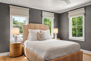 A bedroom with a large bed, two bedside tables, and a window with a view of greenery. - 711 Palm - DOCK - PLUNGE POOL - BIG  YARD - GRILL - FIREPIT (Isle of Palms)