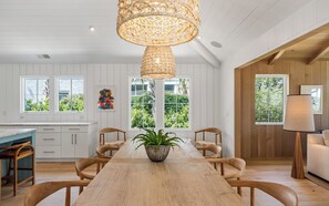 Ett modernt kök med vita köksskåp, ett matbord i trä och en hängande lampa.