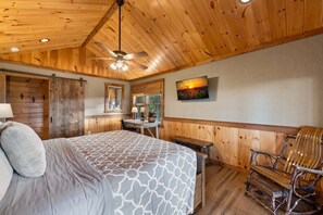 Ein Zimmer mit Holzwandverkleidung, ausgestattet mit einem Bett, einem Schreibtisch, einem Sessel und einem Deckenventilator.