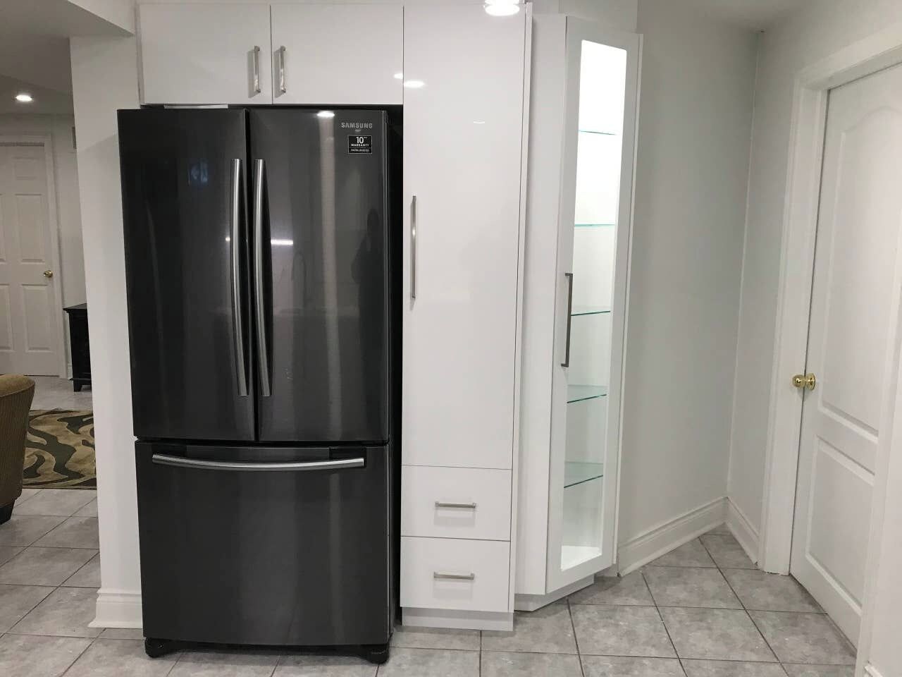 Una cucina moderna con frigorifero nero, mobili bianchi e un pensile in vetro.