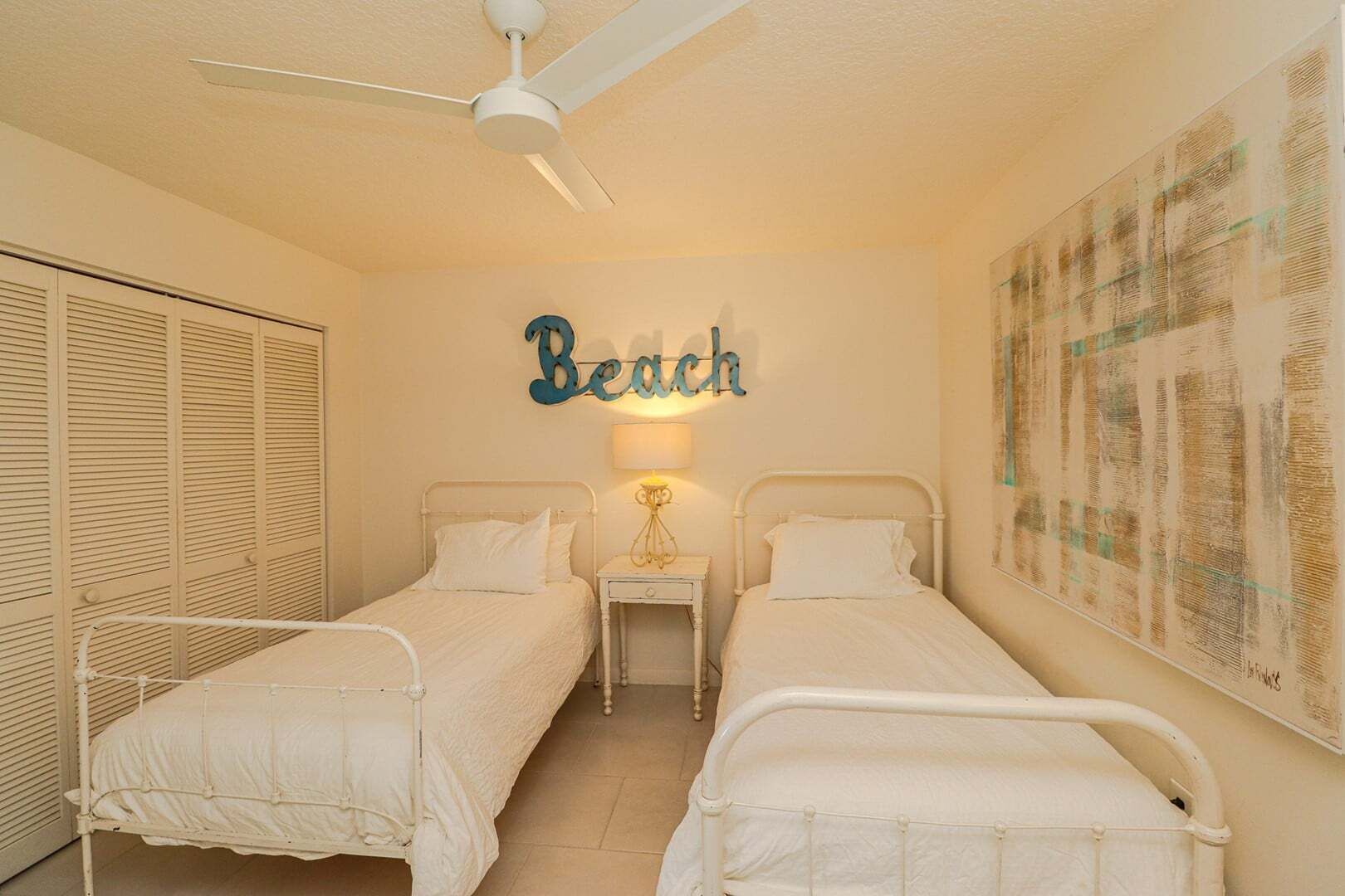 Un dormitorio con dos camas, un ventilador de techo, una lámpara de pared y un cartel que dice 'Beach'.