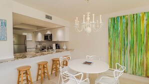 Una cocina moderna con armarios blancos, encimera de granito y comedor con mesa redonda y sillas blancas.