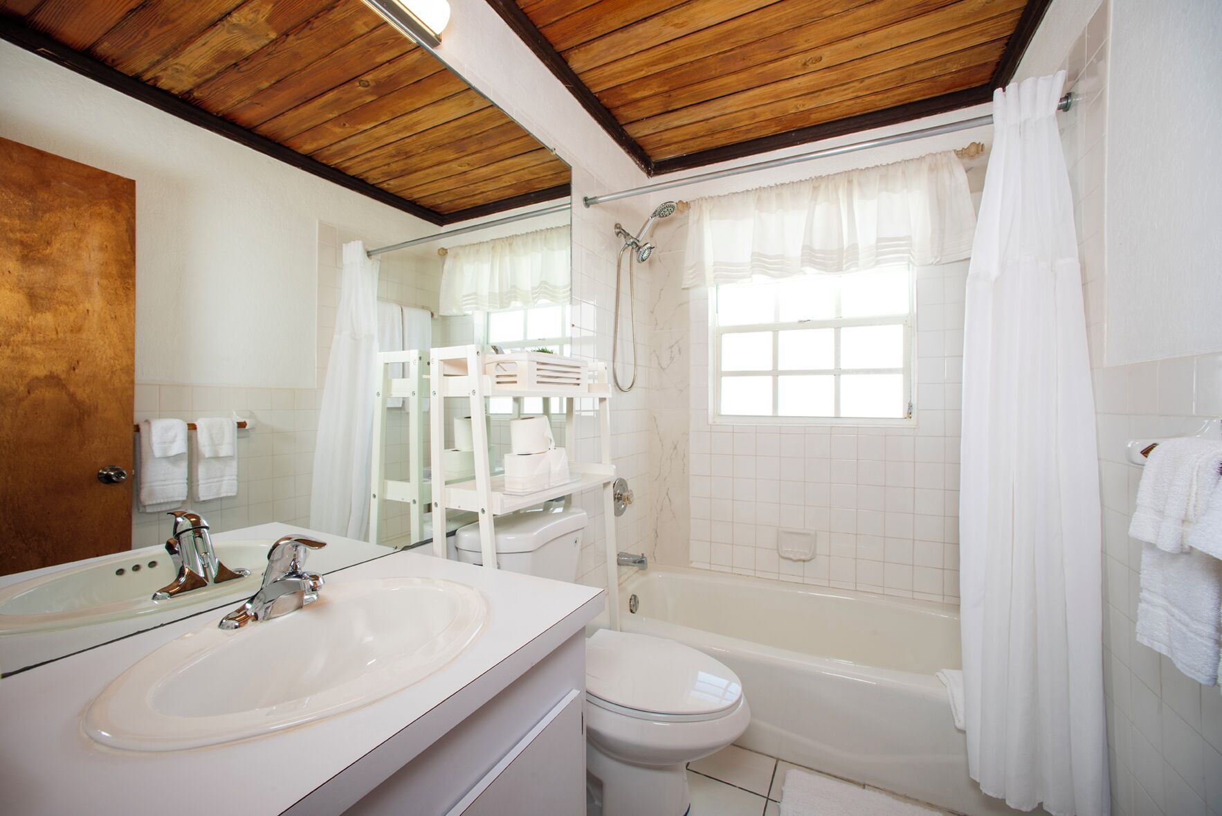 Une salle de bain avec un plafond en bois, une baignoire, une douche, des toilettes et un lavabo avec un miroir.