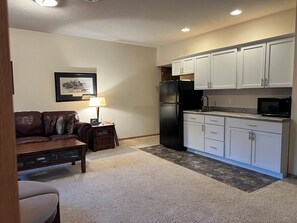 Un espacio habitable compacto con kitchenette, un sofá, una mesita y una lámpara.