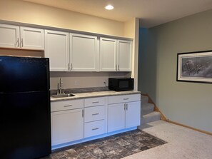 Una cocina con armarios blancos, un refrigerador negro, un microondas y un salpicadero de azulejos.
