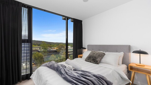 A modern bedroom with a large bed, a view of a cityscape, and a city view through floor-to-ceiling windows. - Stylish City Apartment up to 6 guests with 5 Star amenities (Braddon)