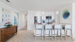 Een moderne keuken met witte kastjes, een centraal eiland met barstoelen, en een groot abstract schilderij aan de muur.