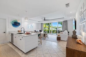 Une cuisine moderne dotée d’un îlot central, d’un coin repas avec un canapé et des chaises, et d’une grande porte-fenêtre coulissante donnant sur un balcon.