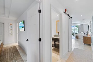 A modern interior with a hallway leading to a bathroom, a living area with a sofa, and a dining area. - Waterfront Bliss in Paradise | Cozy Condo Near Beaches, Dining & More (The Bight Settlement)