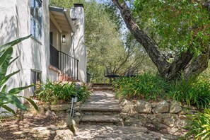 Eine steinerne Treppe führt zu einem modernen Gebäude mit einem Balkon, umgeben von üppiger Vegetation und Bäumen.