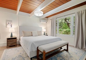 Ein Schlafzimmer mit einem Bett, Nachttischen, einer Bank, einem Fenster mit Vorhängen und einem Deckenventilator.