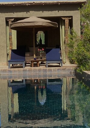 Ein Poolbereich mit zwei Liegestühlen, einem Tisch mit Blumenvase und einer überdachten Sitzgruppe.
