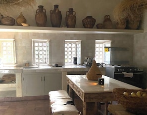 Une cuisine avec des meubles blancs, un fourneau et une fenêtre agrémentée d’un paravent décoratif.